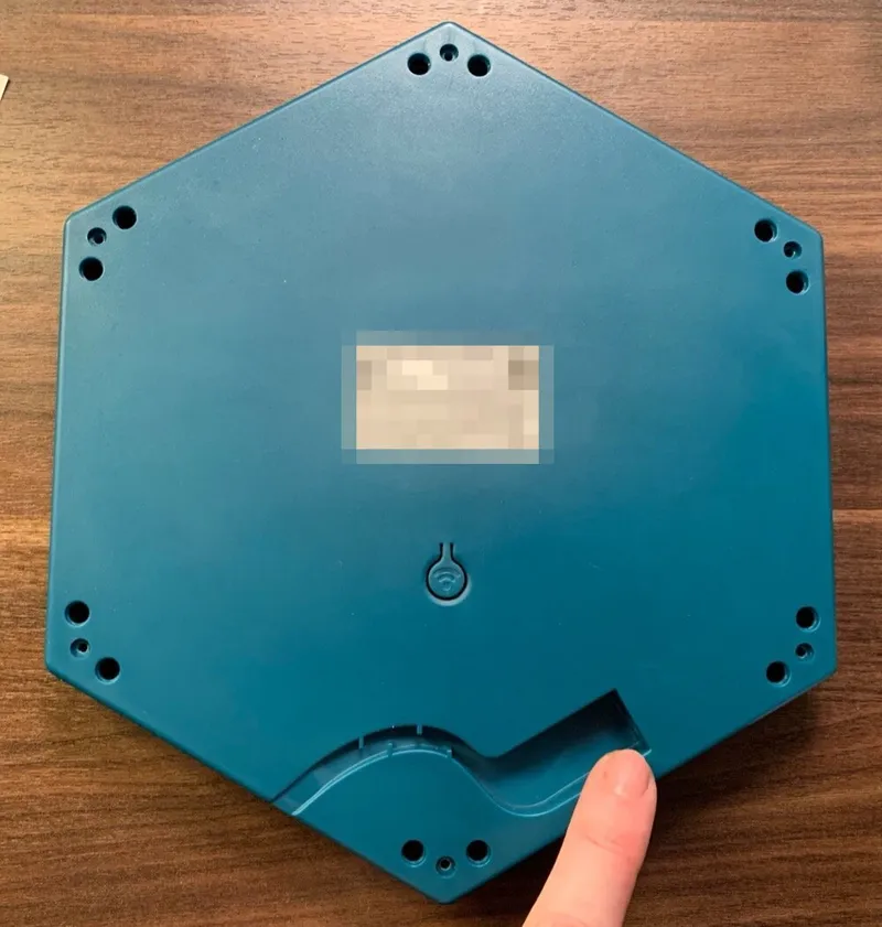 The bottom of a Connect Base, with a finger pointing at the end of the curved cable groove near the edge. The label is blurred.
