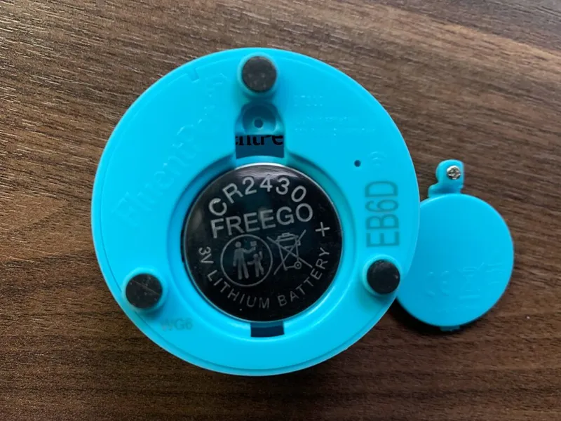 A Connect Button with its battery cover removed, showing a CR2430 coin cell battery with the + side facing out.
